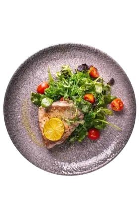 Grilled fish with lemon, cherry tomatoes, and fresh greens on a ceramic plate